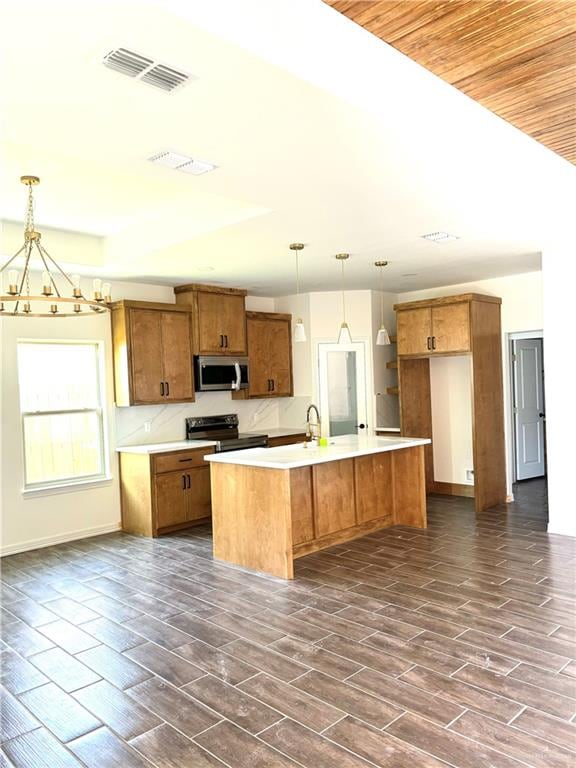 kitchen featuring dark hardwood / wood-style flooring, stainless steel appliances, a kitchen island with sink, decorative light fixtures, and a notable chandelier