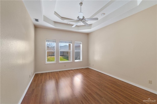 unfurnished room with hardwood / wood-style floors, a tray ceiling, and ceiling fan