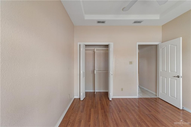 unfurnished bedroom featuring a closet, hardwood / wood-style flooring, a raised ceiling, and ceiling fan