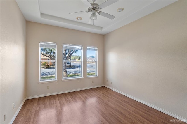 spare room with ceiling fan, a tray ceiling, and hardwood / wood-style floors