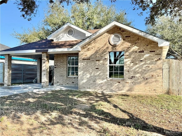 view of front of house featuring driveway, an attached carport, fence, a patio area, and brick siding