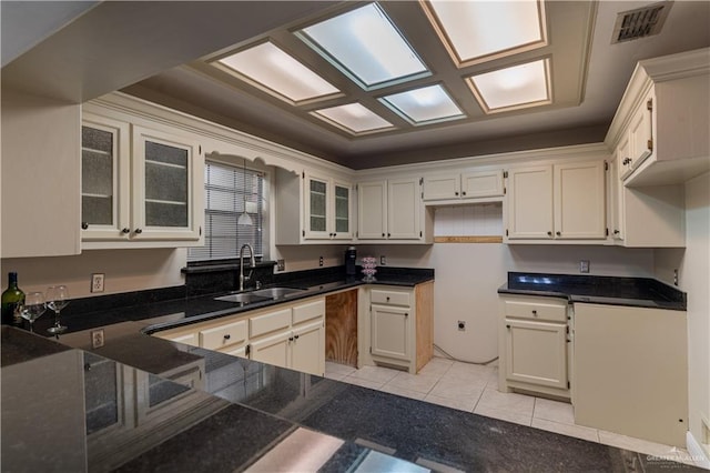 kitchen featuring light tile patterned floors, visible vents, dark stone counters, glass insert cabinets, and a sink