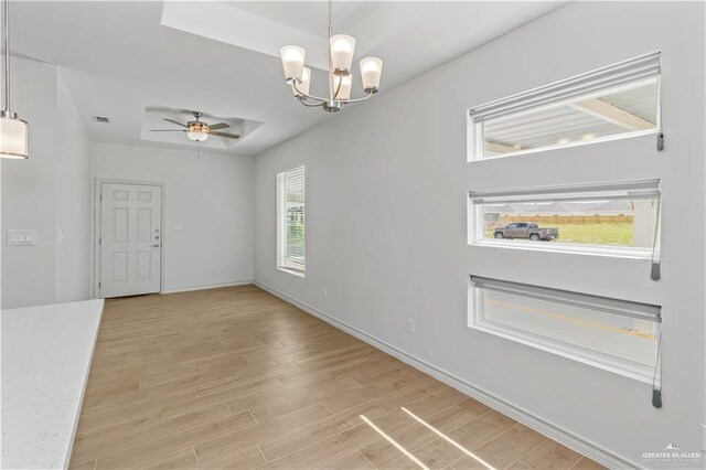 interior space featuring visible vents, baseboards, a tray ceiling, light wood-style flooring, and ceiling fan with notable chandelier