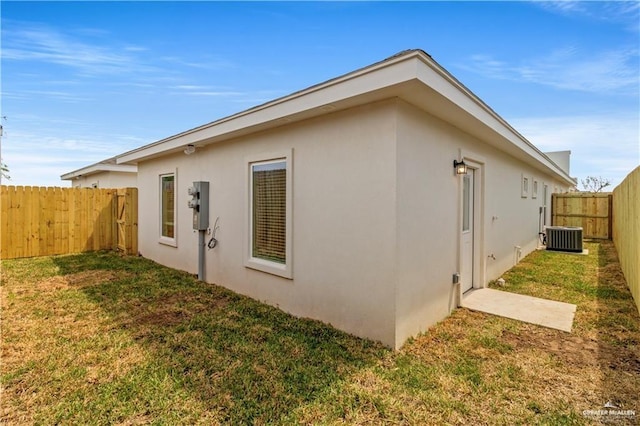 view of side of property with central air condition unit, a lawn, a fenced backyard, and stucco siding