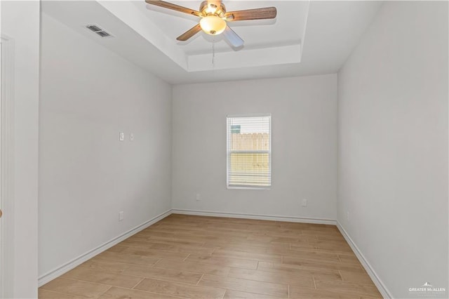 unfurnished room with light wood-type flooring, visible vents, a ceiling fan, baseboards, and a raised ceiling