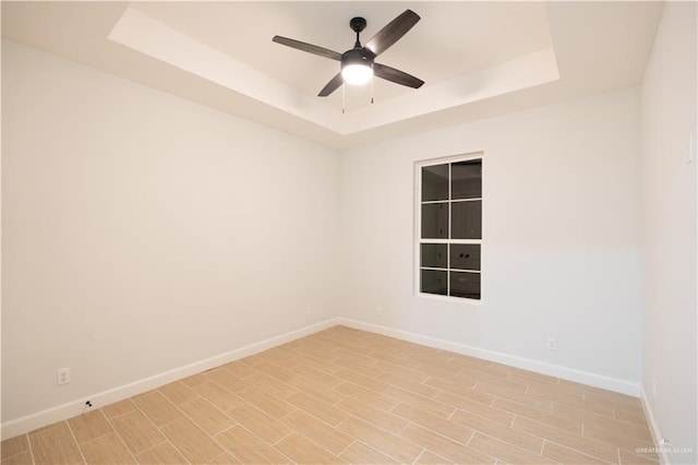 unfurnished room featuring a raised ceiling, ceiling fan, and light hardwood / wood-style floors