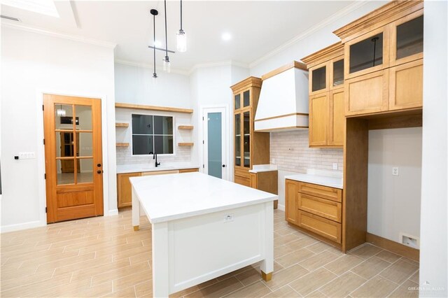 kitchen with pendant lighting, custom exhaust hood, sink, tasteful backsplash, and a kitchen island