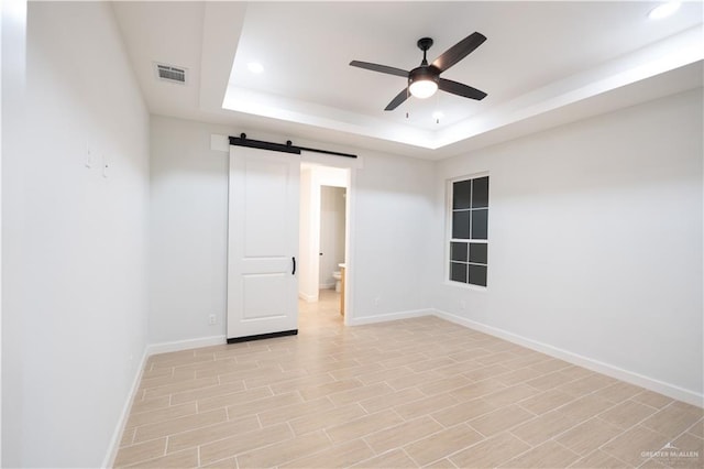 spare room with ceiling fan, a barn door, a raised ceiling, and light wood-type flooring