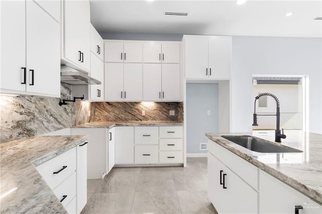 kitchen with white cabinets, decorative backsplash, light stone counters, and sink