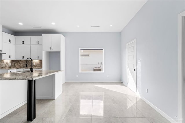 kitchen with backsplash, exhaust hood, sink, light stone countertops, and white cabinetry