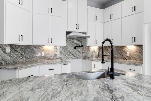 kitchen with backsplash, ventilation hood, white cabinets, sink, and light stone counters