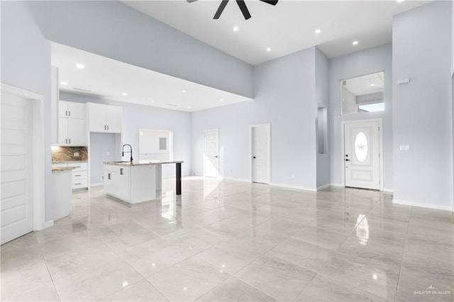 unfurnished living room with a towering ceiling, ceiling fan, and sink