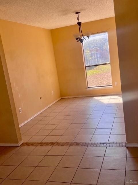 unfurnished room with a chandelier, a textured ceiling, baseboards, and light tile patterned floors