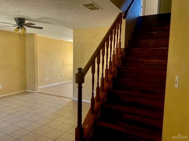 stairway with ceiling fan, a textured ceiling, visible vents, baseboards, and tile patterned floors