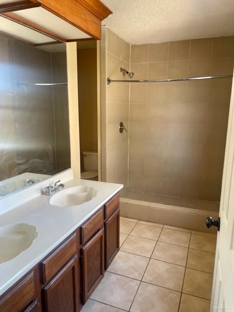 bathroom with double vanity, toilet, tile patterned floors, a textured ceiling, and a sink