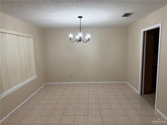 empty room with a chandelier, a textured ceiling, light tile patterned flooring, visible vents, and baseboards