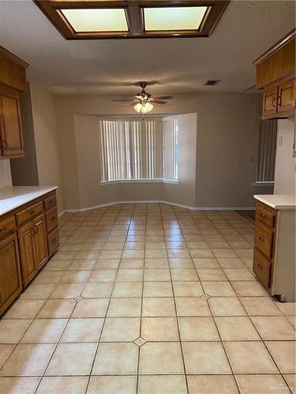 kitchen with brown cabinetry, light countertops, a textured ceiling, and light tile patterned floors