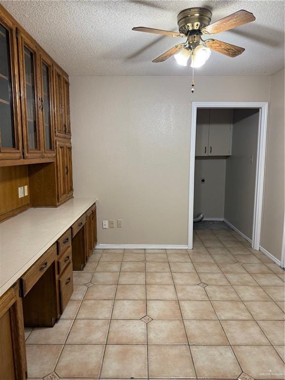 unfurnished office featuring light tile patterned floors, baseboards, built in study area, ceiling fan, and a textured ceiling