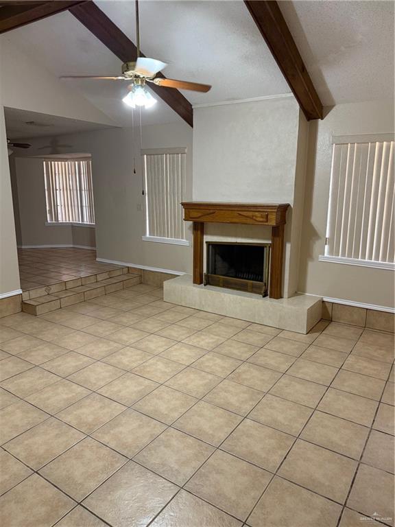 unfurnished living room featuring light tile patterned floors, baseboards, a fireplace with raised hearth, ceiling fan, and vaulted ceiling with beams