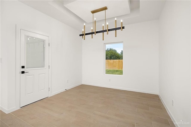 spare room with a notable chandelier, a raised ceiling, and light wood-type flooring