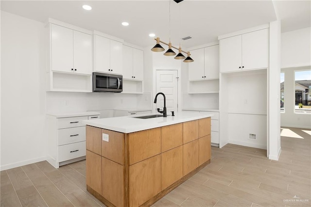 kitchen with sink, hanging light fixtures, light hardwood / wood-style floors, a center island with sink, and white cabinets