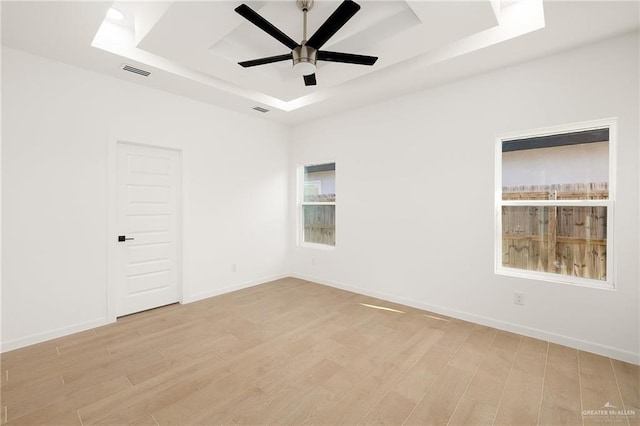 empty room with ceiling fan, light hardwood / wood-style floors, and a tray ceiling