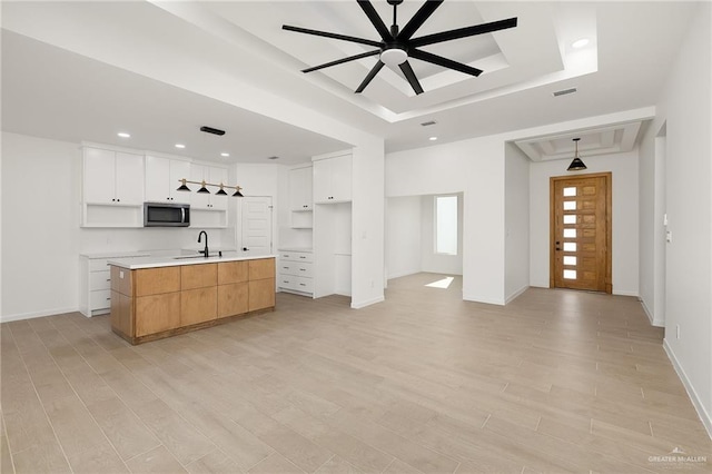 kitchen with a large island with sink, sink, white cabinets, and light wood-type flooring