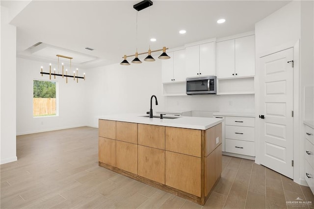 kitchen featuring a kitchen island with sink, white cabinets, sink, hanging light fixtures, and light wood-type flooring