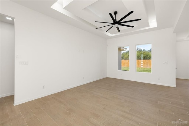 spare room with light hardwood / wood-style floors, ceiling fan, and a tray ceiling