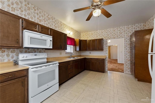 kitchen with a sink, wallpapered walls, white appliances, ceiling fan, and light countertops