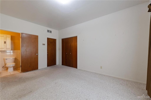 unfurnished bedroom featuring ensuite bath, carpet, visible vents, and multiple closets