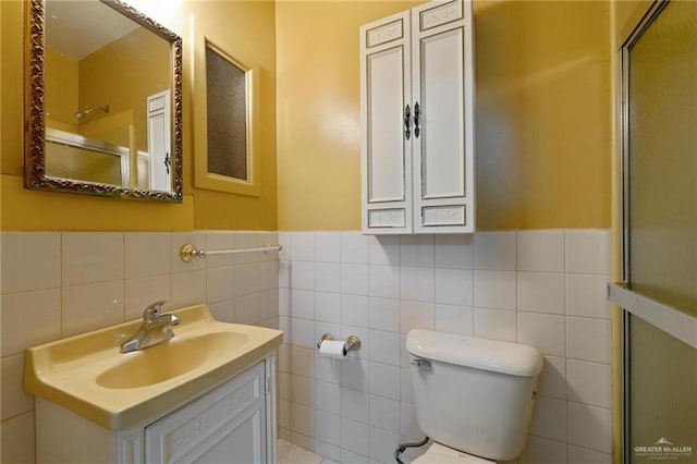 full bathroom featuring a shower with shower door, toilet, vanity, tile walls, and wainscoting