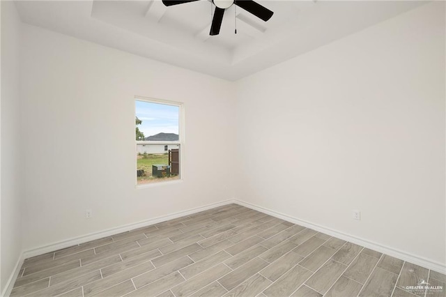 unfurnished room with ceiling fan, light wood-type flooring, and a tray ceiling