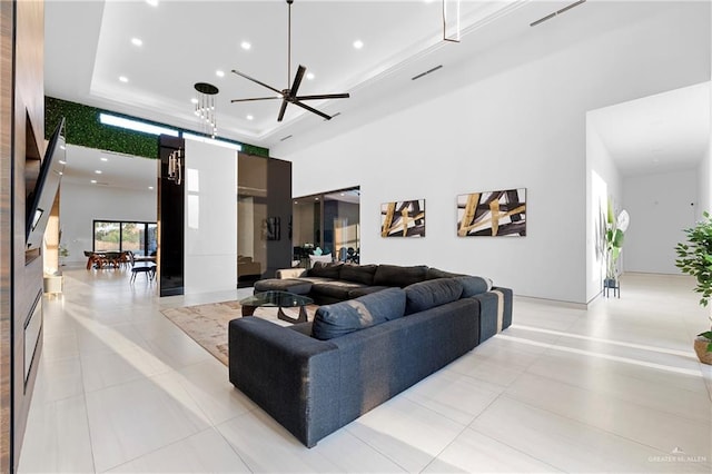 living room with a tray ceiling, light tile patterned floors, a towering ceiling, and ceiling fan