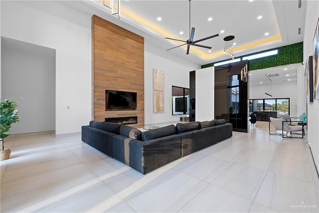 tiled living room featuring ceiling fan, a towering ceiling, a fireplace, and a tray ceiling