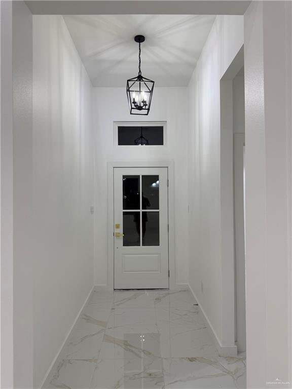 entryway featuring baseboards, a chandelier, and light marble finish flooring