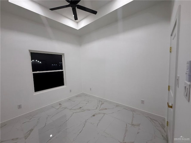 empty room featuring a ceiling fan, baseboards, marble finish floors, and a raised ceiling