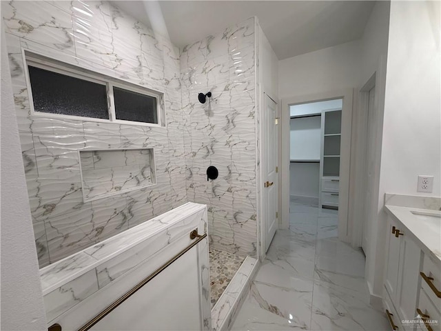 bathroom with marble tiled floors, a tile shower, a walk in closet, and vanity