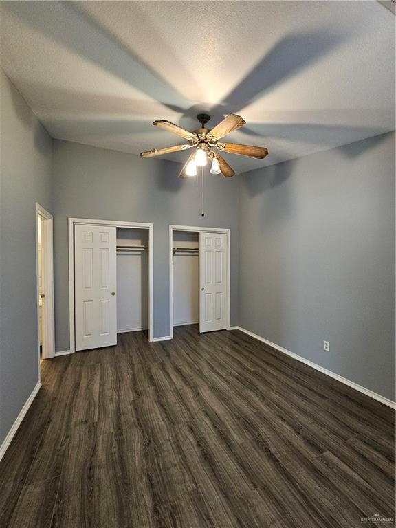 unfurnished bedroom with a high ceiling, dark hardwood / wood-style flooring, multiple closets, and ceiling fan