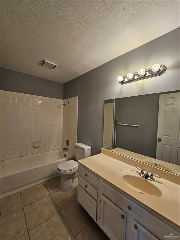 full bathroom with a textured ceiling, toilet, tile patterned floors, vanity, and tiled shower / bath combo