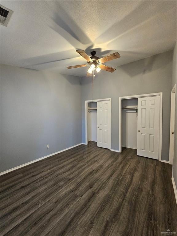 unfurnished bedroom featuring ceiling fan, two closets, a textured ceiling, and dark hardwood / wood-style floors