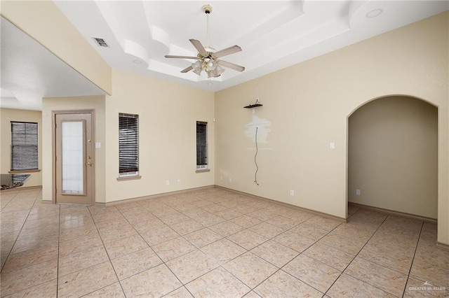 tiled empty room featuring a raised ceiling and ceiling fan