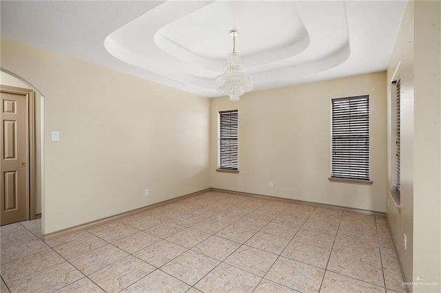 tiled empty room featuring a chandelier and a raised ceiling