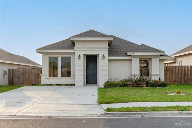 view of front of property with roof with shingles, a front yard, fence, and stucco siding