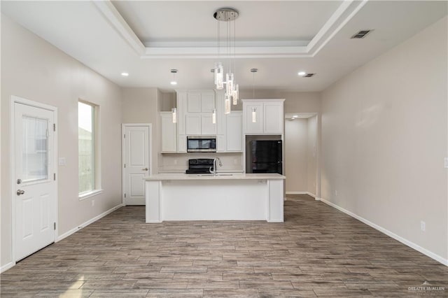 kitchen featuring a tray ceiling, visible vents, black appliances, and wood finished floors