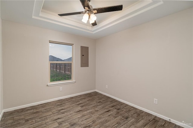 spare room featuring a tray ceiling, electric panel, baseboards, and wood finished floors