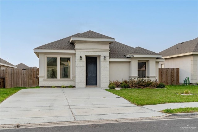 view of front of property with a shingled roof, a front yard, fence, and stucco siding