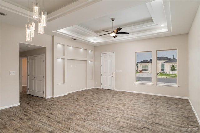 empty room featuring a tray ceiling, wood finished floors, and a ceiling fan