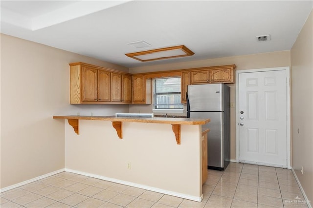 kitchen featuring kitchen peninsula, stainless steel fridge, a kitchen breakfast bar, and light tile patterned flooring