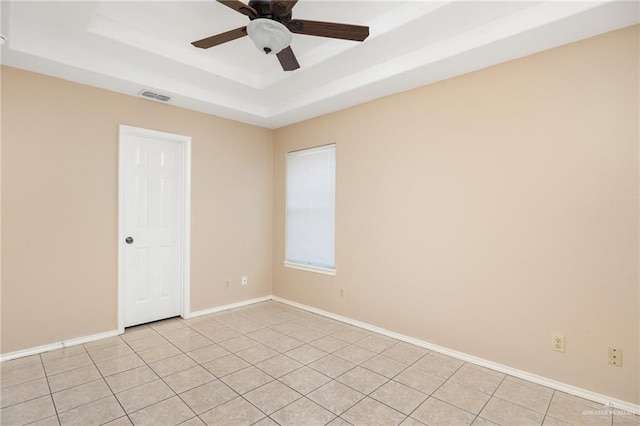 spare room featuring a raised ceiling, ceiling fan, and light tile patterned flooring